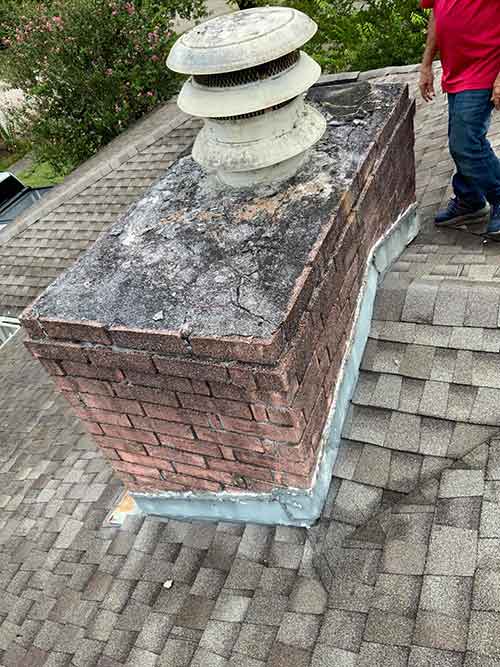 Chimney crown crumbling and black with smoke damage on top of composition shingles