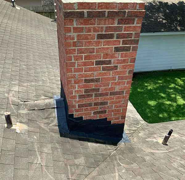 Nice brick chimney with verigated colors of red with new black flashing installed and green grass in background.