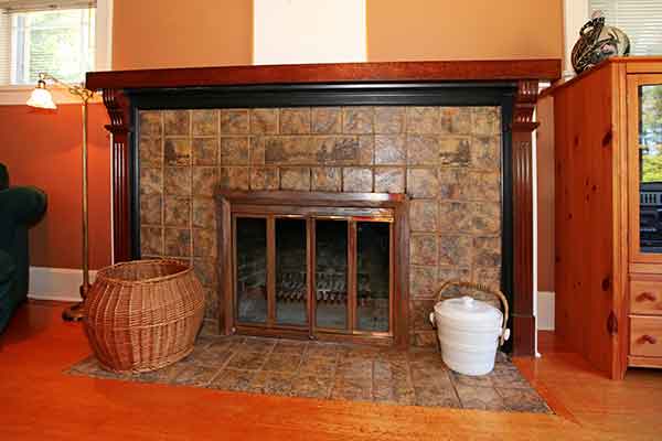 Fireplace Glass Doors-tile surround with dark wood mantel-Floor lamp-basket on left-crock on right.