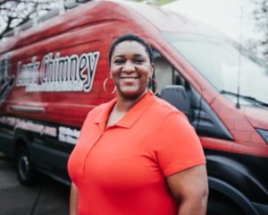 Ieshia Wilson Technician with red shirt and large hoop earrings and company truck in the background with logohimney