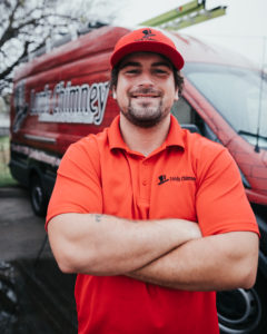 Johnathan Alvey Technician with red logo shirt as well as hat and company truck with logo in the background.