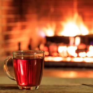 a clear mug of cider sitting in front of a lit fireplace