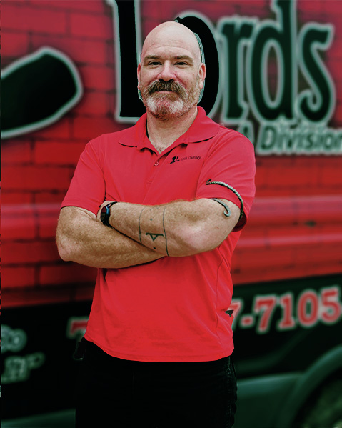 Craig Domak wearing a red Lords Chimney shirt and black pants. He is standing in front of the Lords Chimney van.