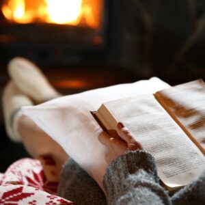 someone warming their feet by a fireplace while reading a book
