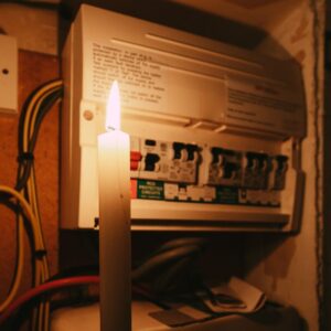 a lit white candle held up to a fuse box in the dark