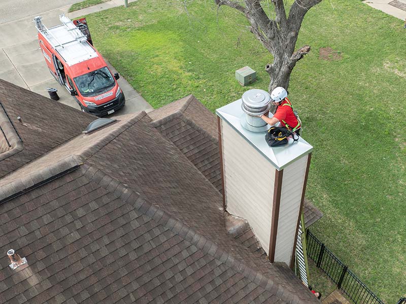 Lords Chimney- Original image chimney repairs Technician wearing a helmet and harness replacing a chimney cap